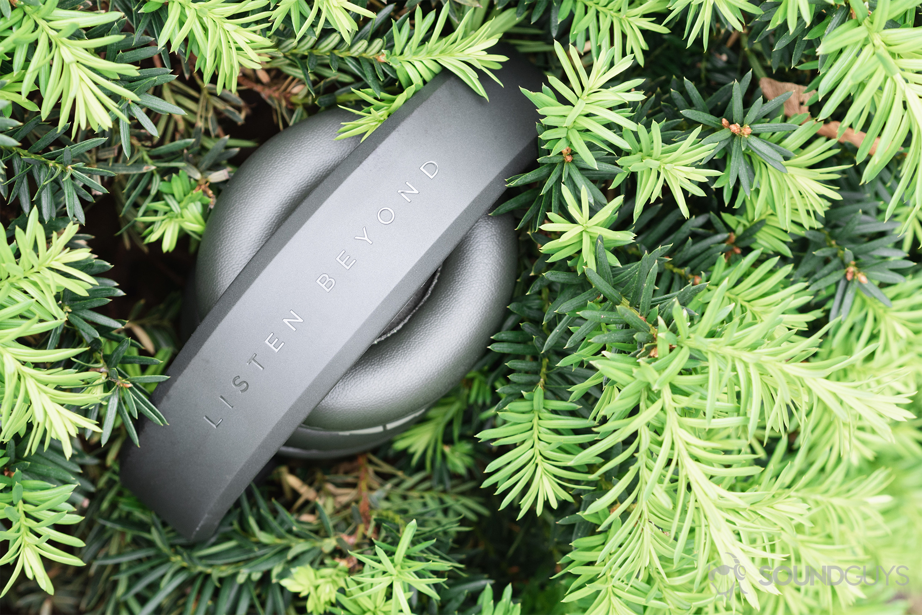 Focal Listen Wireless review: The headphones (olive) folded up and resting in a bright green shrub.