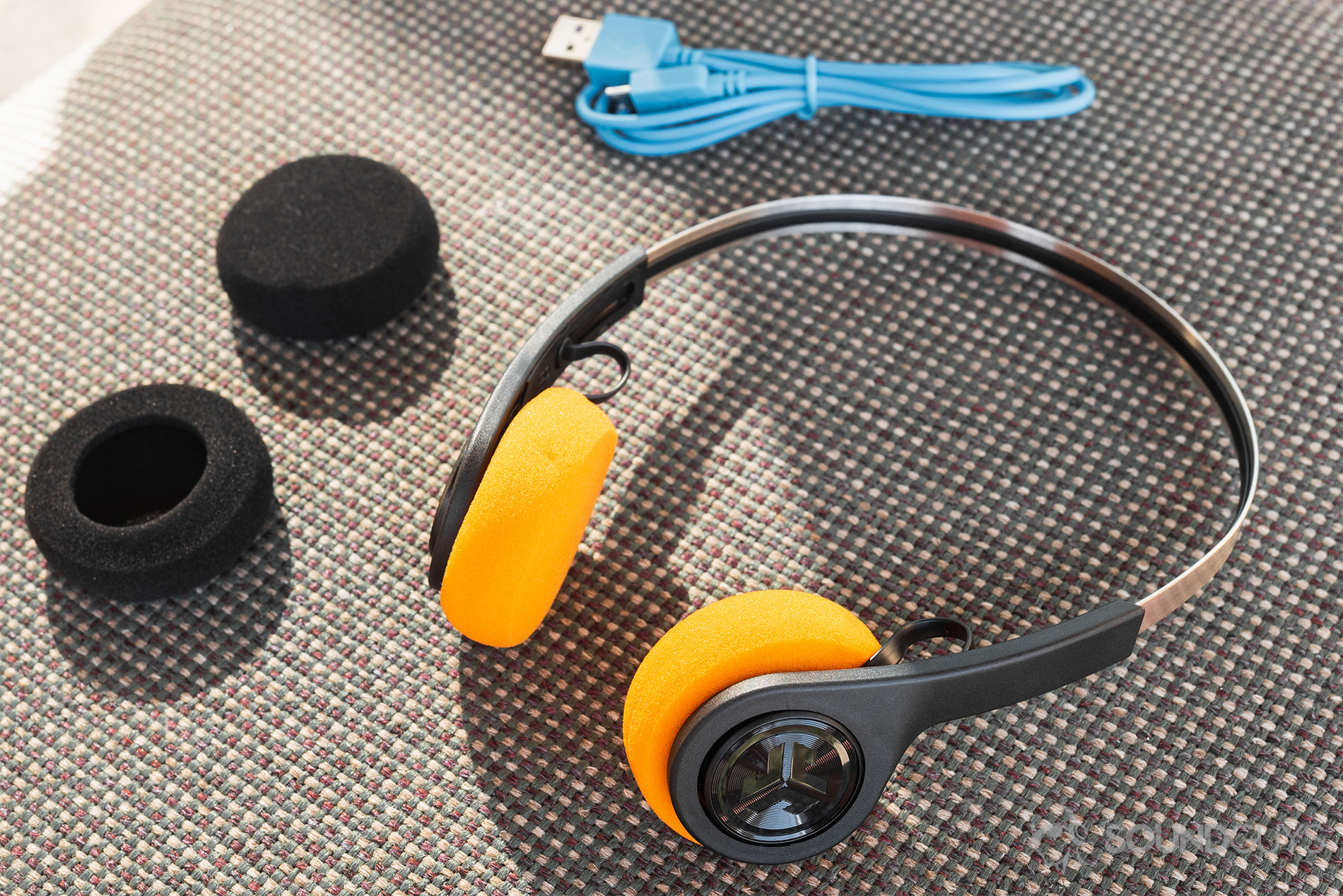 JLab Rewind Wireless Retro: The headphones with the alternative ear pads and blue micro-USB on a fabric surface.