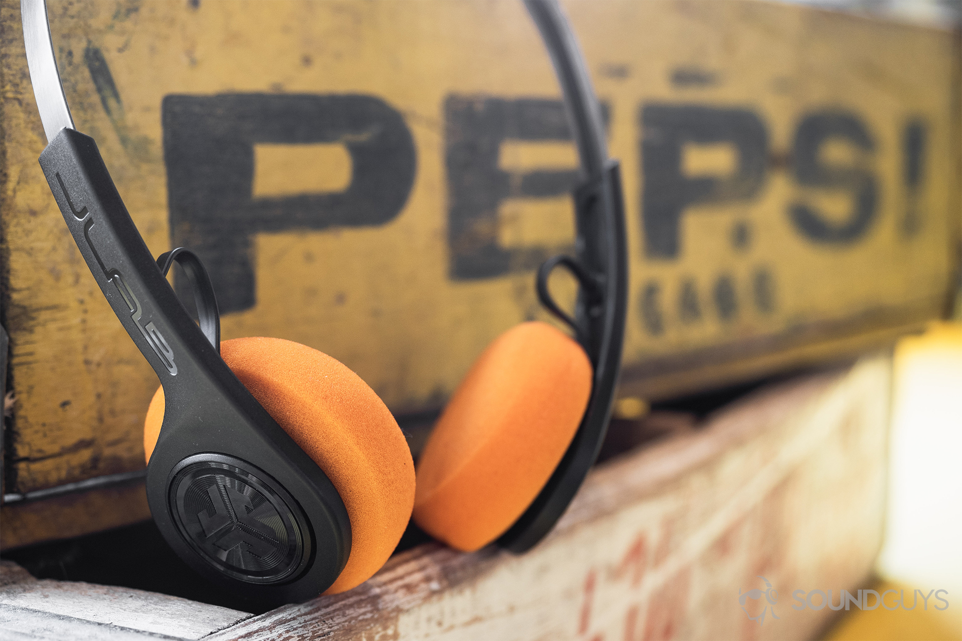 JLab_Audio Rewind Wireless Retro_LK_8 JLab Rewind Wireless Retro: The headphones propped on a wooden box and against another labeled "Pepsi."