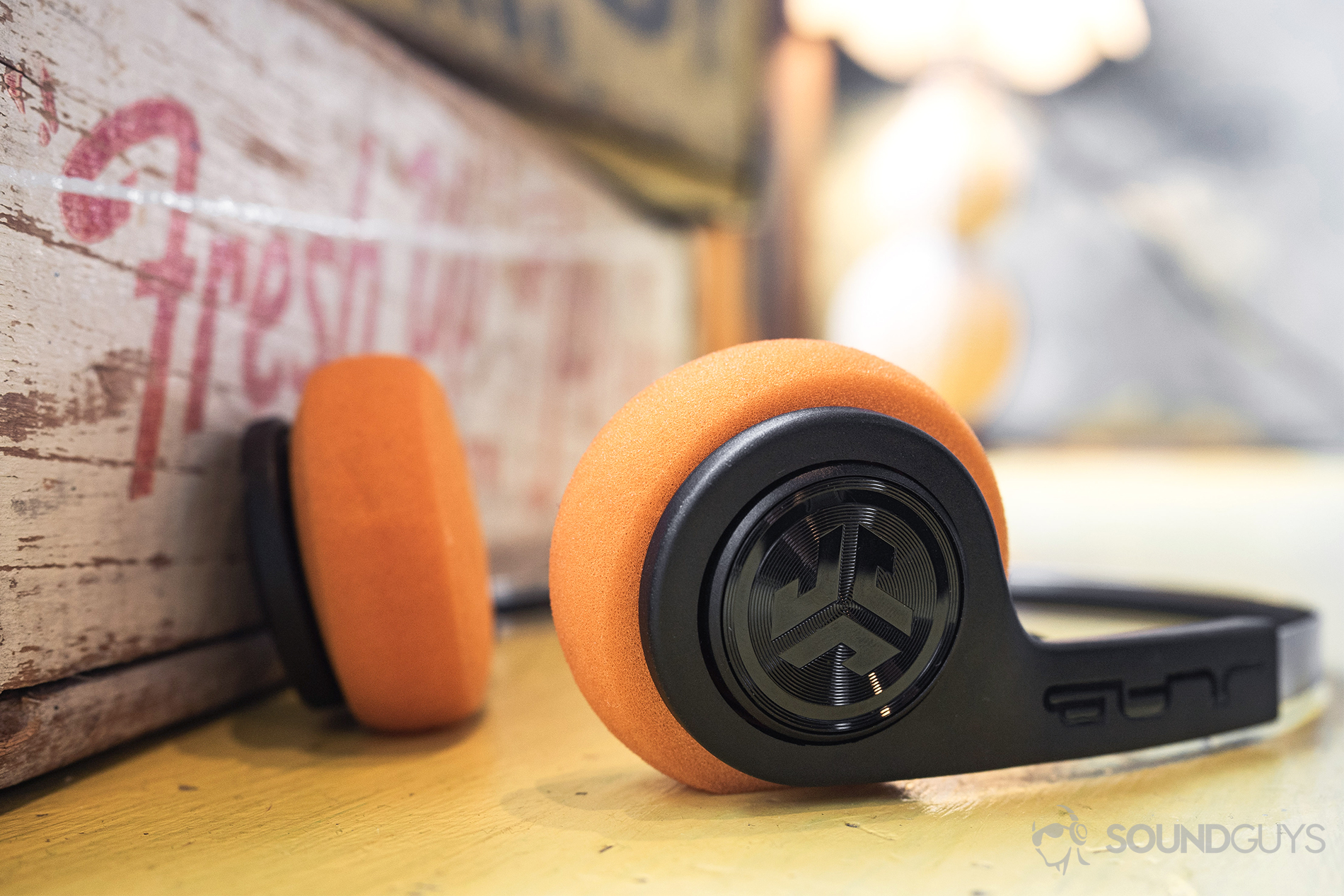 JLab Rewind Wireless Retro: The headphones laying flat on a table in front of some worn apple boxes.
