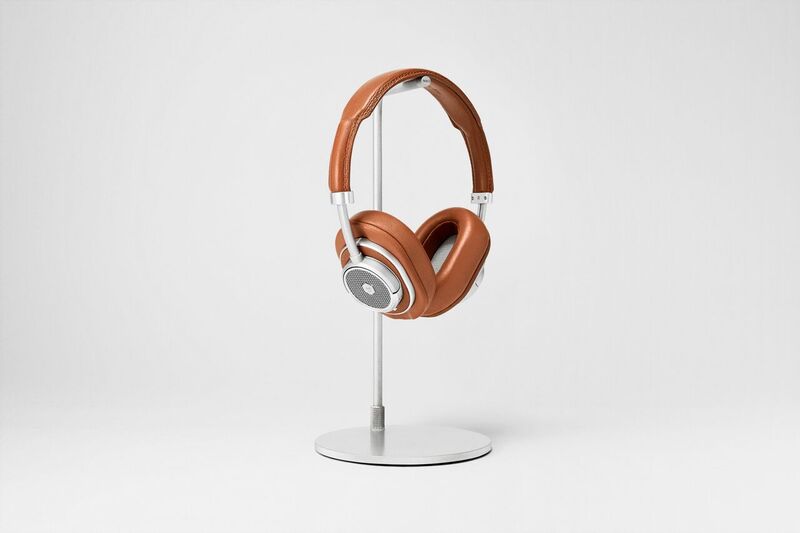 Master &amp; Dynamic MW50+: The brown version of the headphones with the over-ear pads installed. The headphones are on a silver headphone stand against a light-gray background.