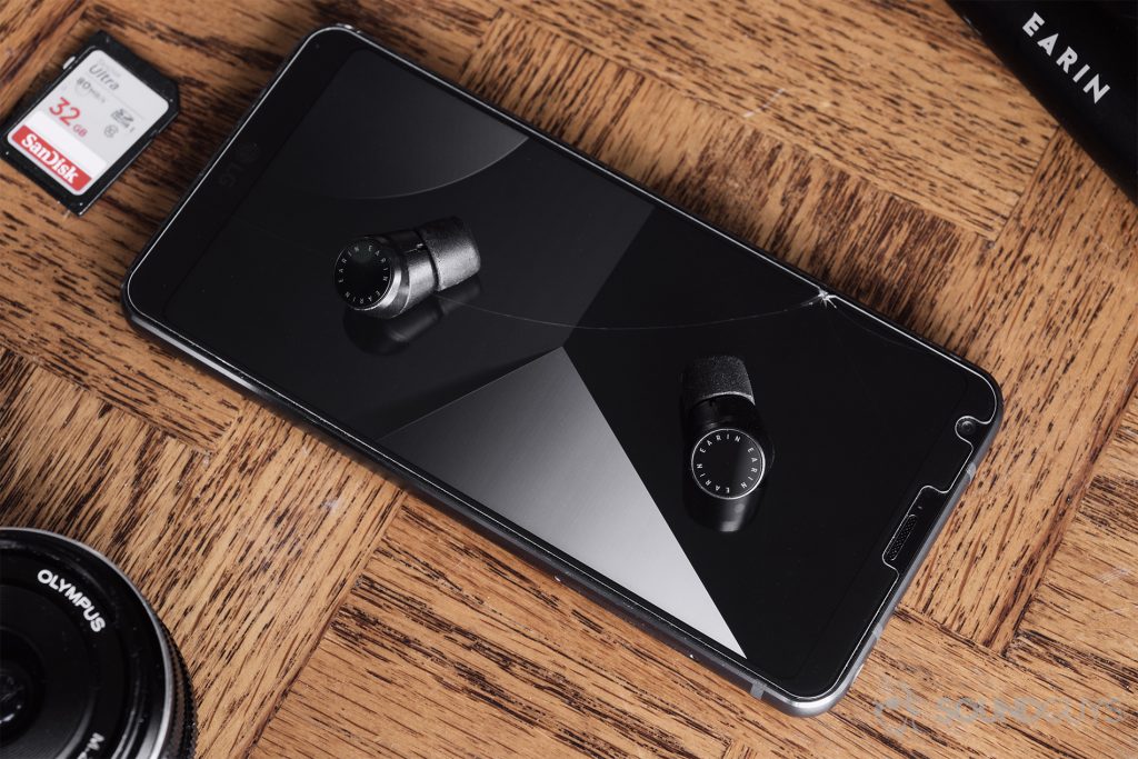 AirPods alternatives - Earin M-2 review: The earbuds resting on an LG G6 on a wood backgorund.