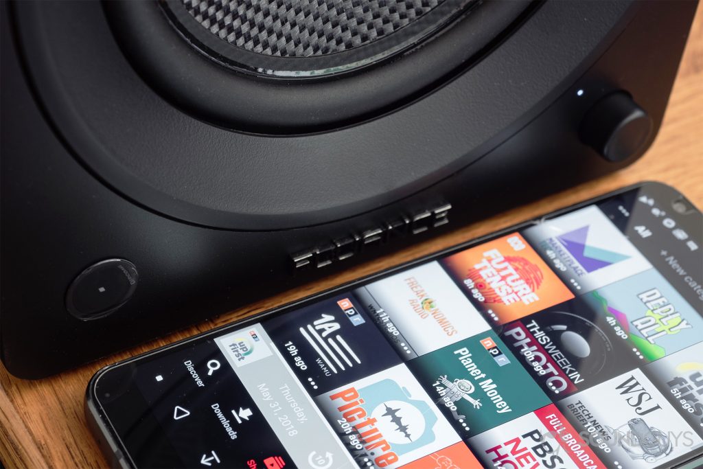 Fluance Ai40 review: A close-up of the bottom of the active speaker with a phone next to it. A podcast app is open.