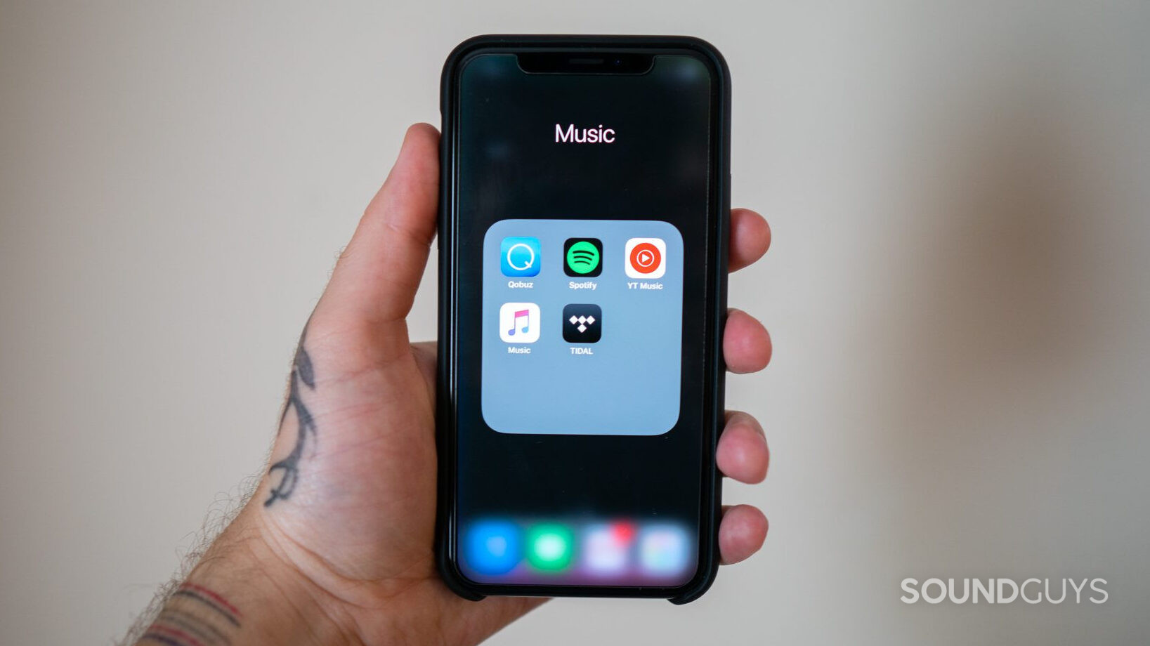 A hand holds an iPhone that displays a folder of music streaming service applications.