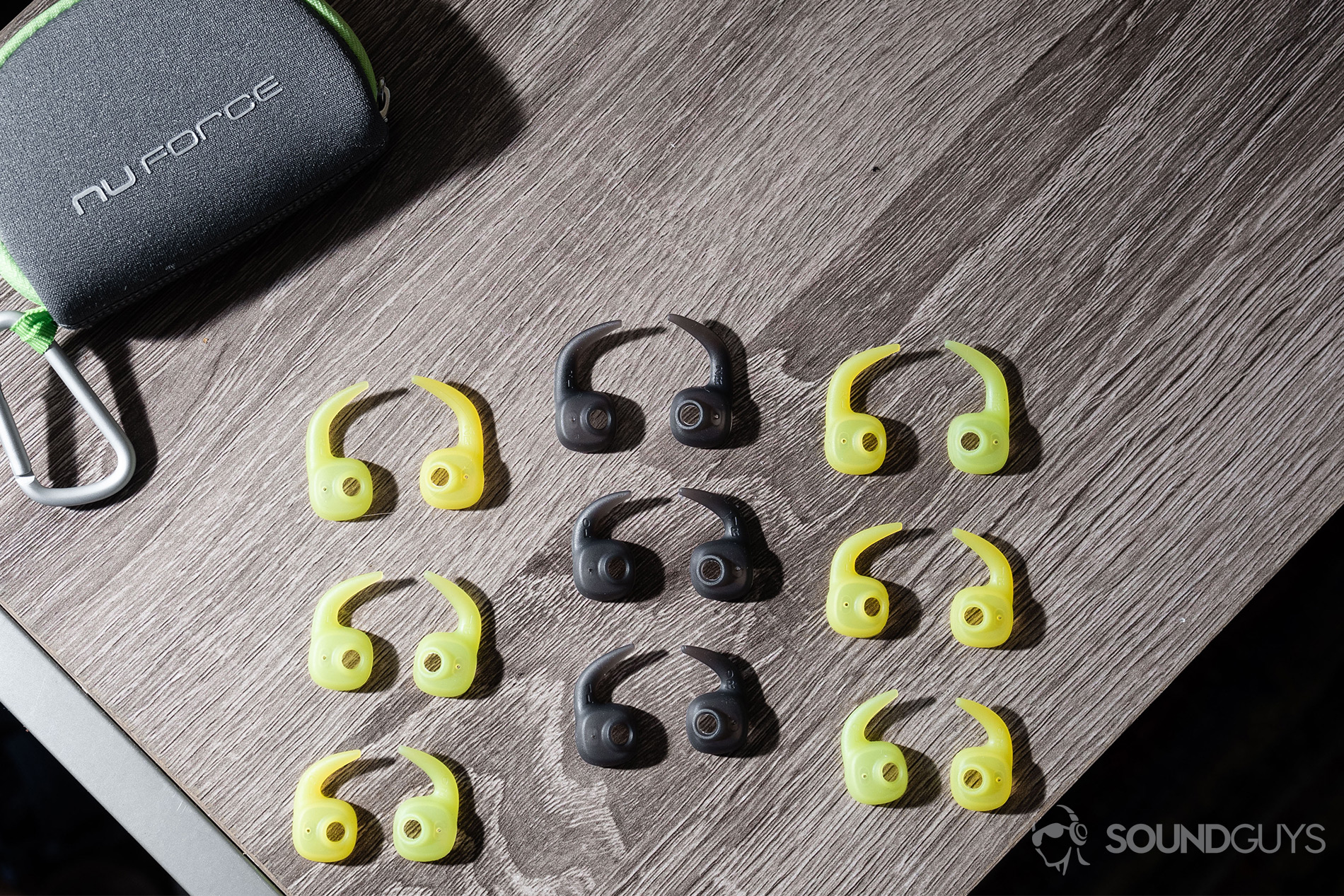 Optoma NuForce_Be Sport4-2 Optoma NuForce Be Sport4: The zipper carying case/carabiner and nine pairs of wing tips on a wooden surface.