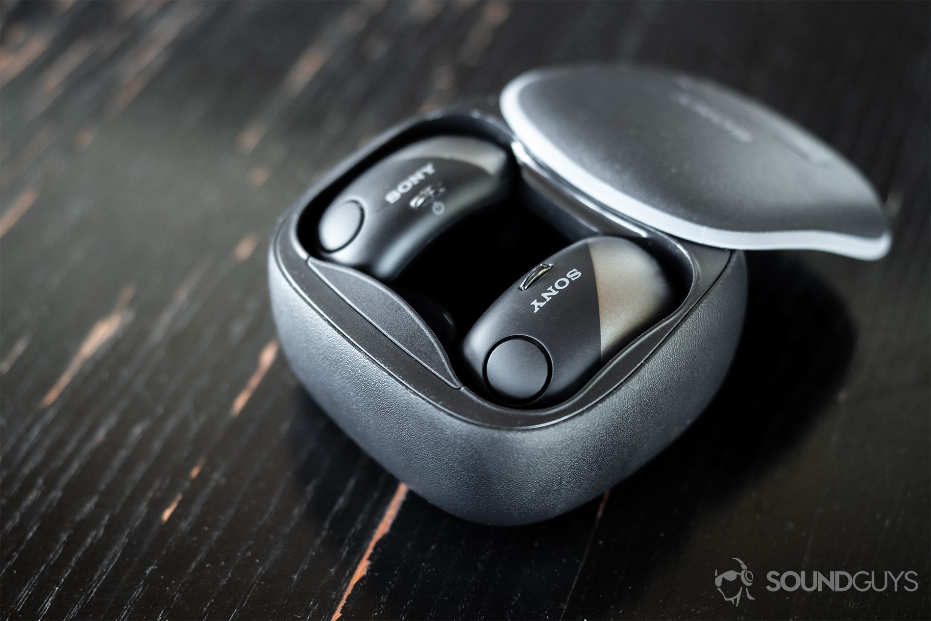 Sony WF-SP700N: A downward facing image of both true wireless earbuds docked in the charging case on a rustic, black wood surface.
