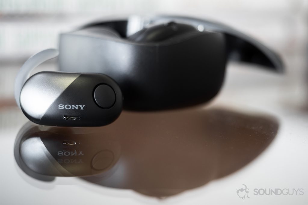 Sony WF-SP700N: One earbud is out of the case on a glass table while the other is docked in the case behind.