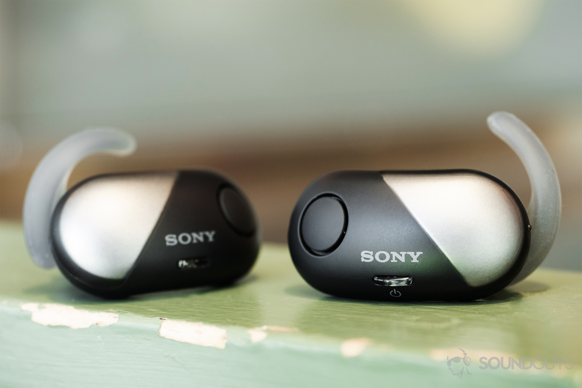 Sony WF-SP700N: The two earbuds front-facing on a green wooden railing.