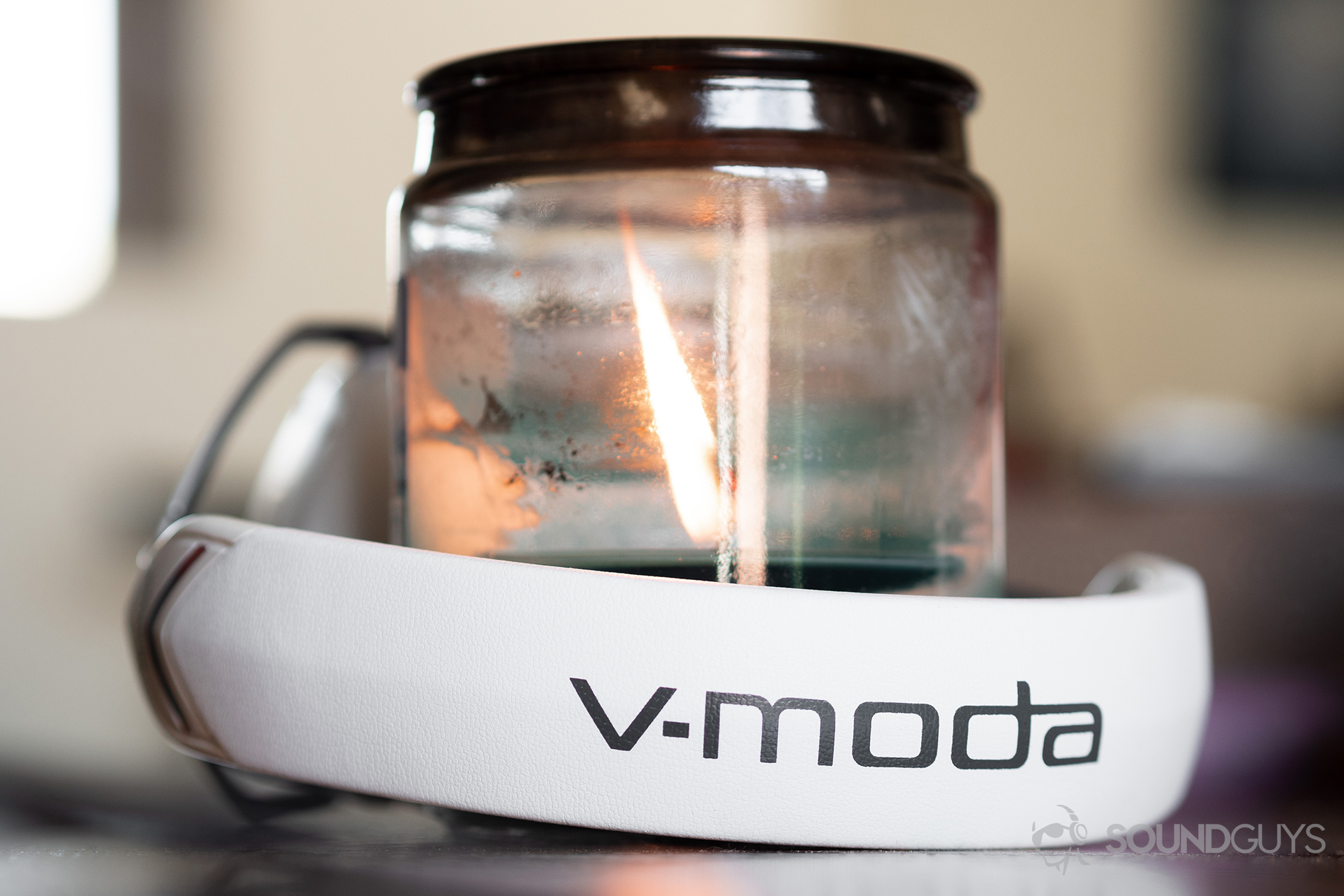 The V-Moda Crossfade 2 Codex headphones wrapped around a large candle/holder. The headband is facing the camera and reads "V-Moda."