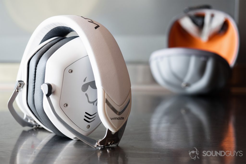 The V-Moda Crossfade 2 Codex headphones folded up but standing on a reflective surface wtih teh clam shell Exoskeleton case in the background.