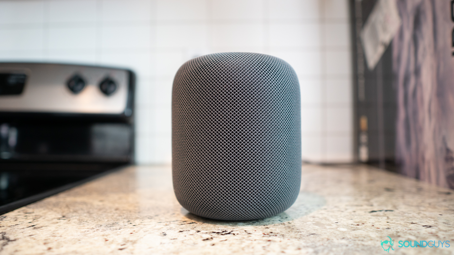 The Apple Homepod pictured on a marble kitchen countertop.