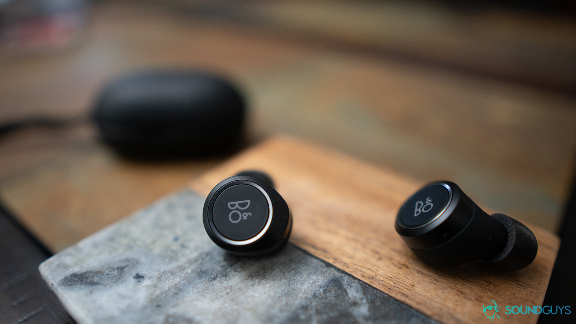 Close-up shot of both earbuds on a coaster with the charging case in the background. 