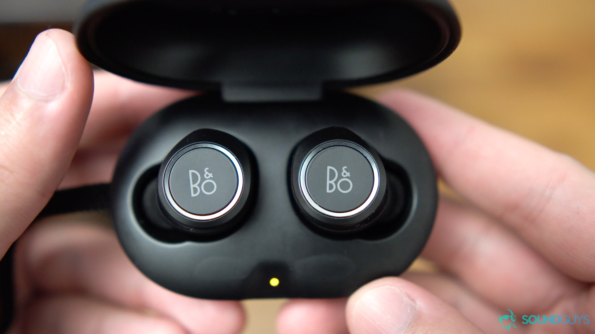 The charging case of the Beoplay E8 held open in hand so the earbuds are clearly visible.