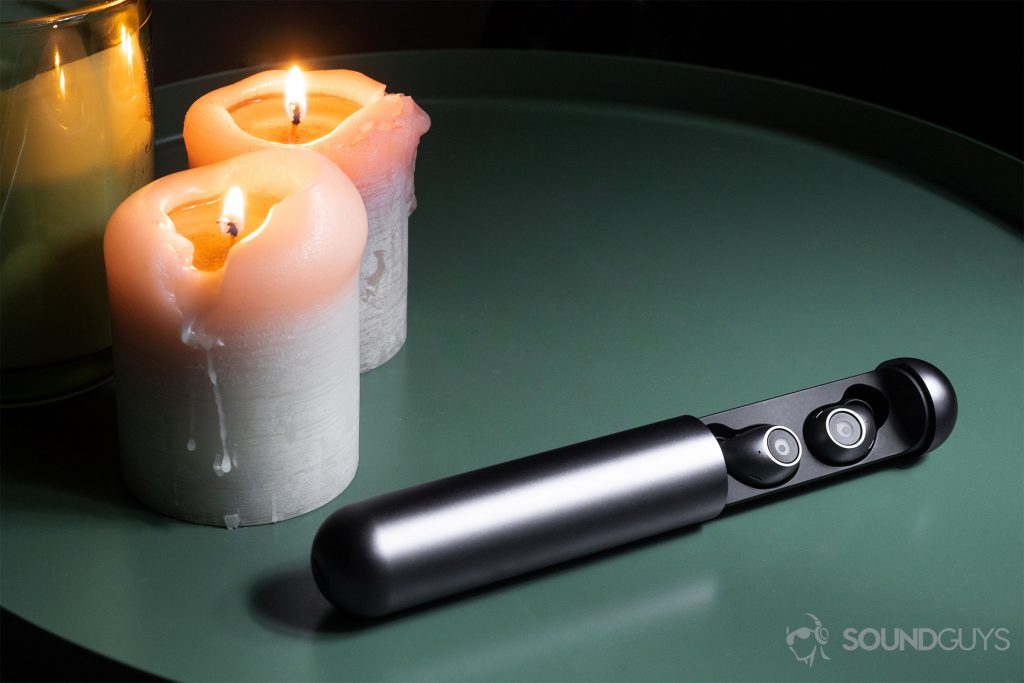 Best workout earbuds: The earbuds resting in the open carrying case. There are three candles to the back left of the image, two of which ar lit. The objects are on a green end table.