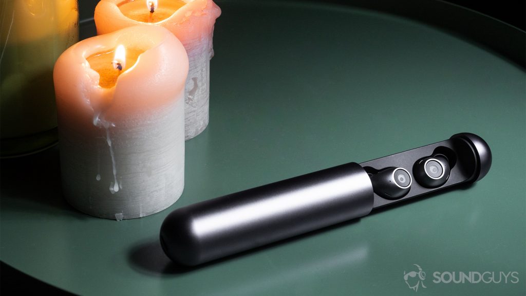 Best workout earbuds: The earbuds resting in the open carrying case. There are three candles to the back left of the image, two of which ar lit. The objects are on a green end table.