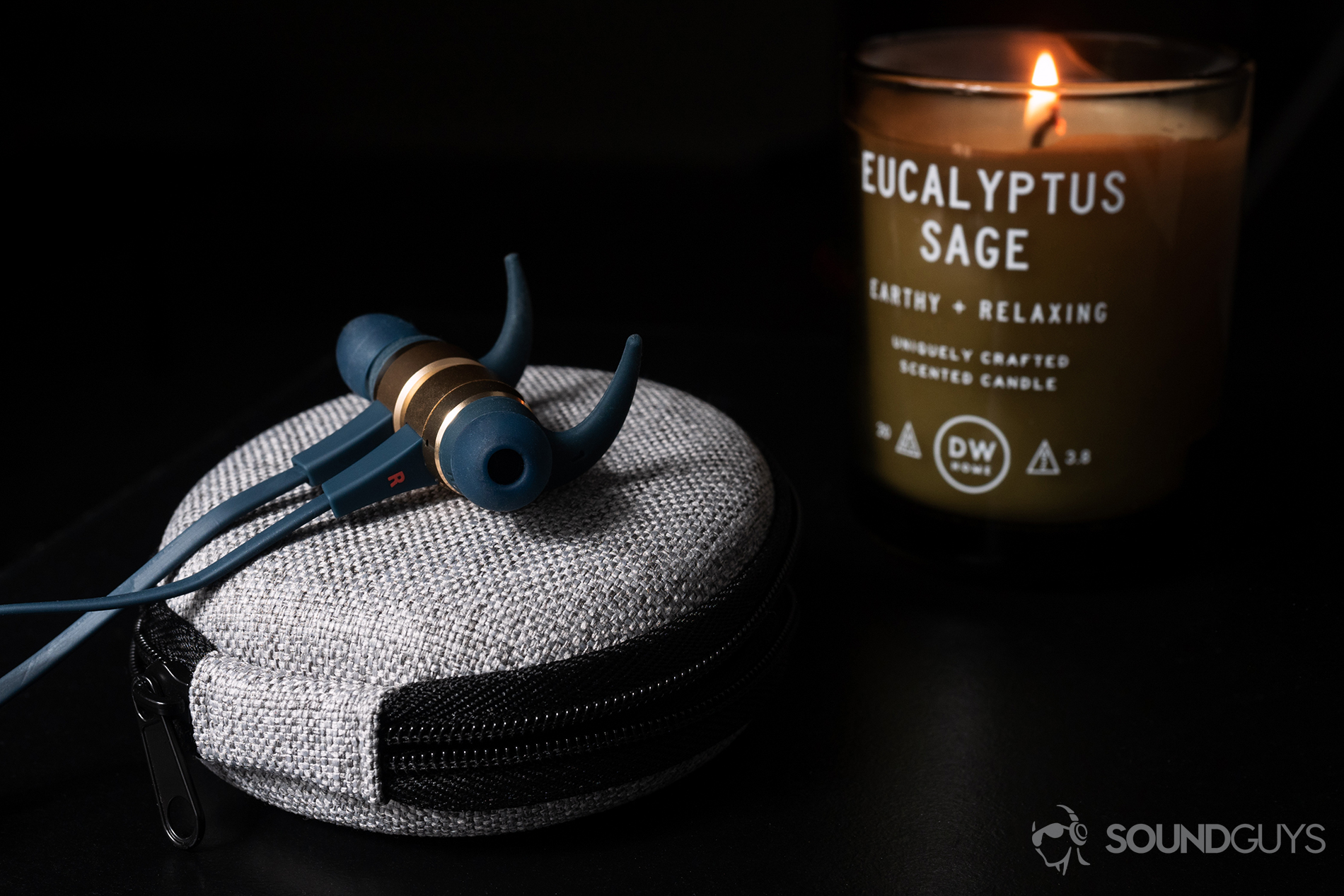 Optoma NuForce Be Live5: The earbuds on top of the included grey carrying case with a lit candle in the background.