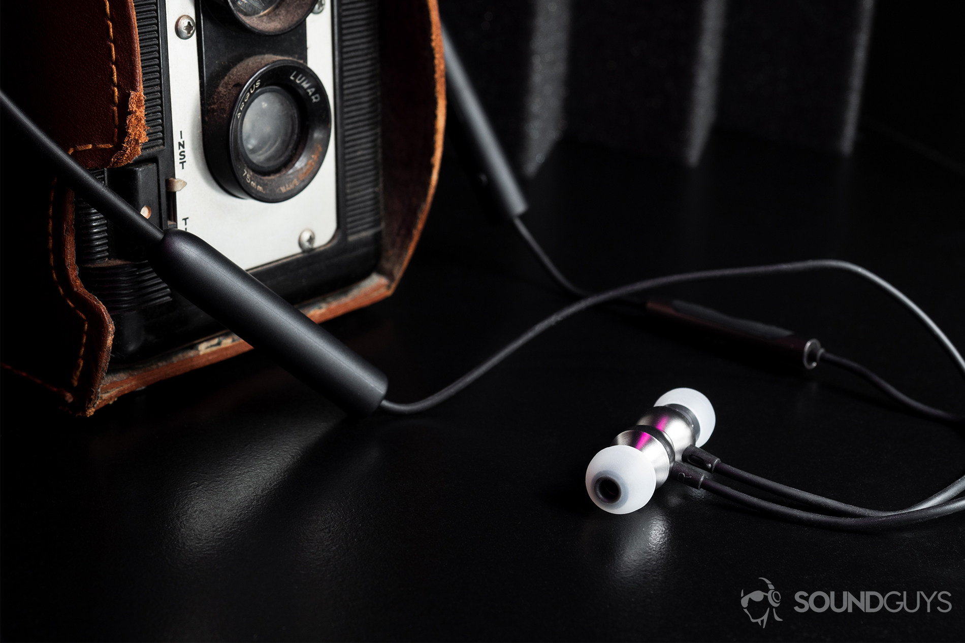 RHA MA390 Wireless: An image of the earbuds wrapped around a film camera. The earbuds are hooked together via the magnetic housings.