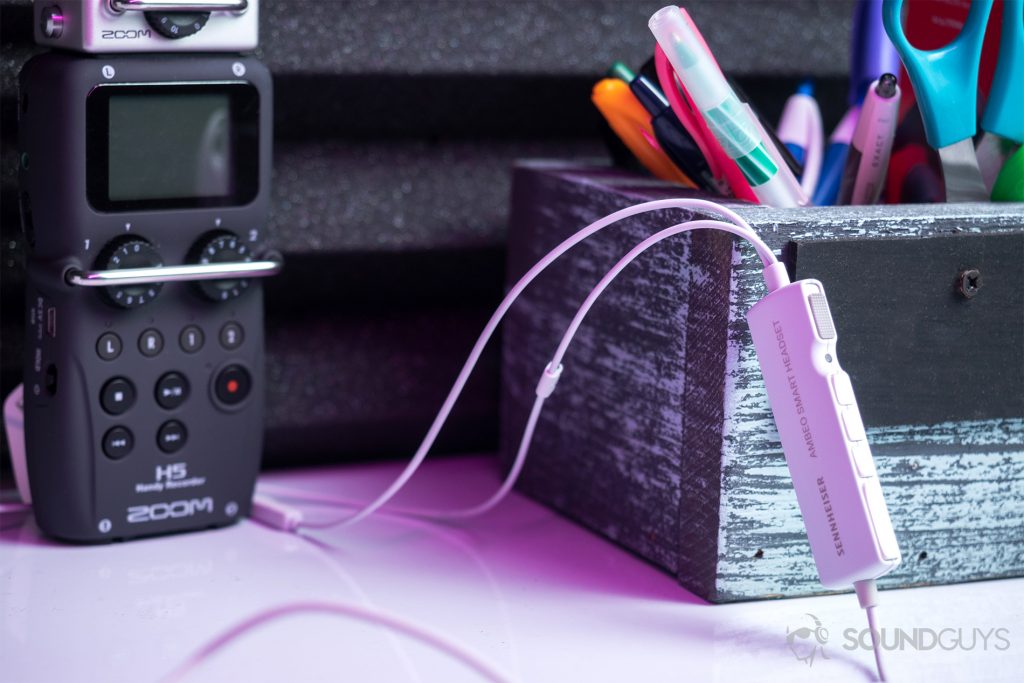 Sennheiser Ambeo Headset: The headset's control module leaning up against a box full of pens. A Zoom H5 recorder is in the background and the image is lit by a magenta LED.