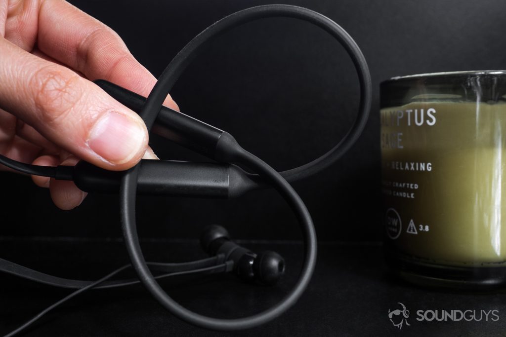 A photo of the BeatsX neckband flexing multiple directions with an unlit candle in the background on a black background.