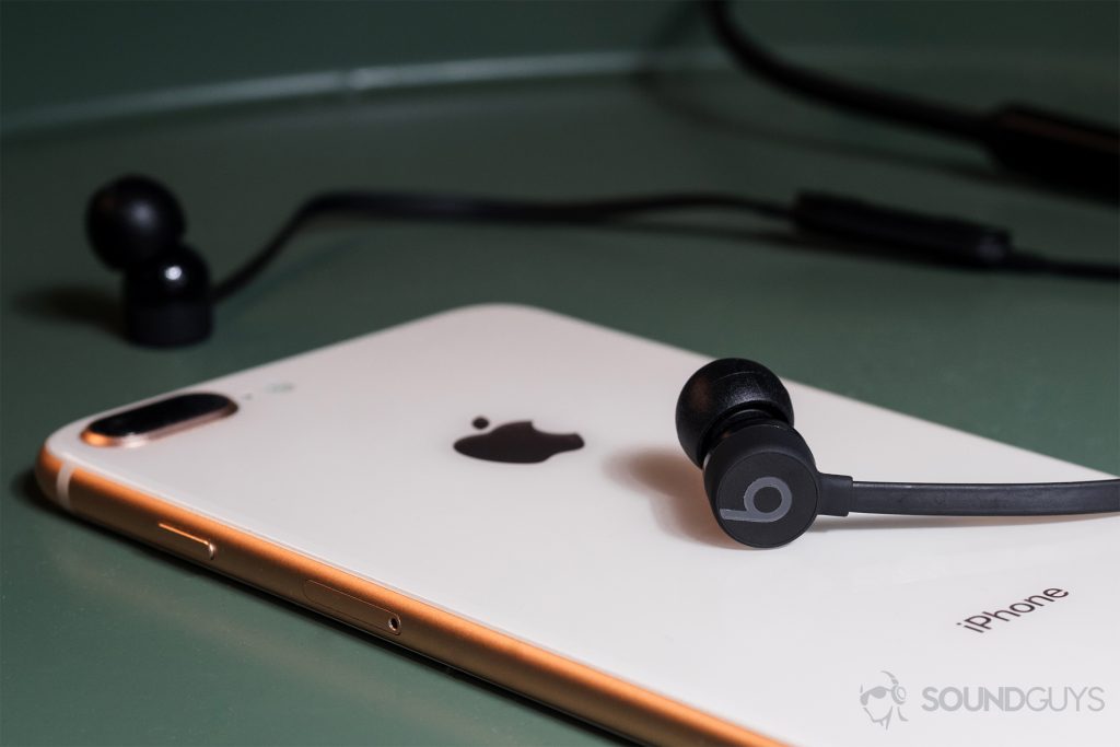 BeatsX review: The BeatsX on an iPhone 8 Plus in rose gold both resting on a green end table.