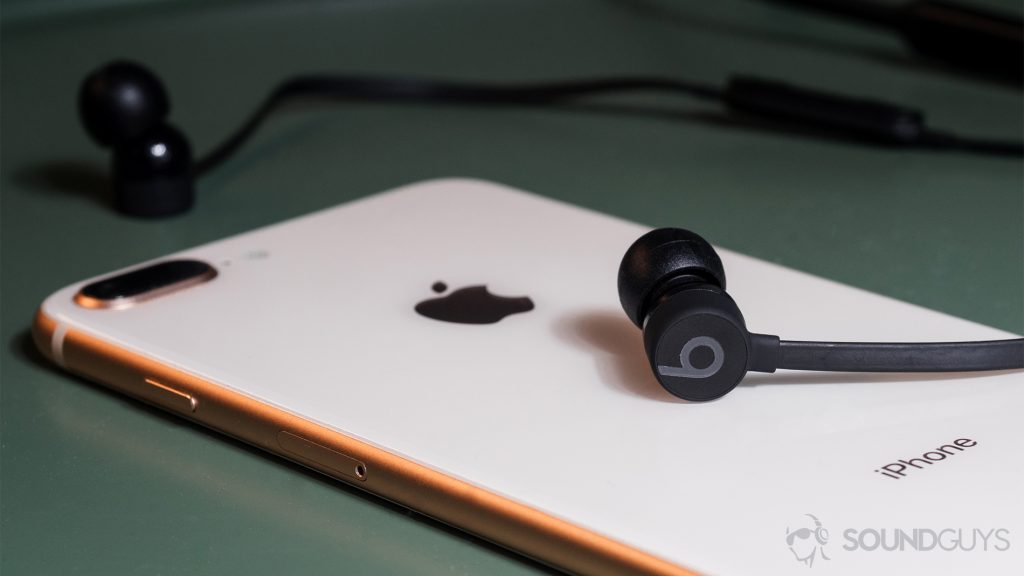 A photo of the BeatsX on an iPhone 8 Plus in rose gold both resting on a green end table.