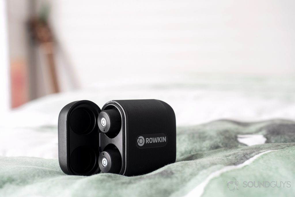 Rowkin Ascent Micro: The earbuds are in the case which is slightly angled awaay from the lens. It rests on a bed with a guitar neck blurred out in the background.