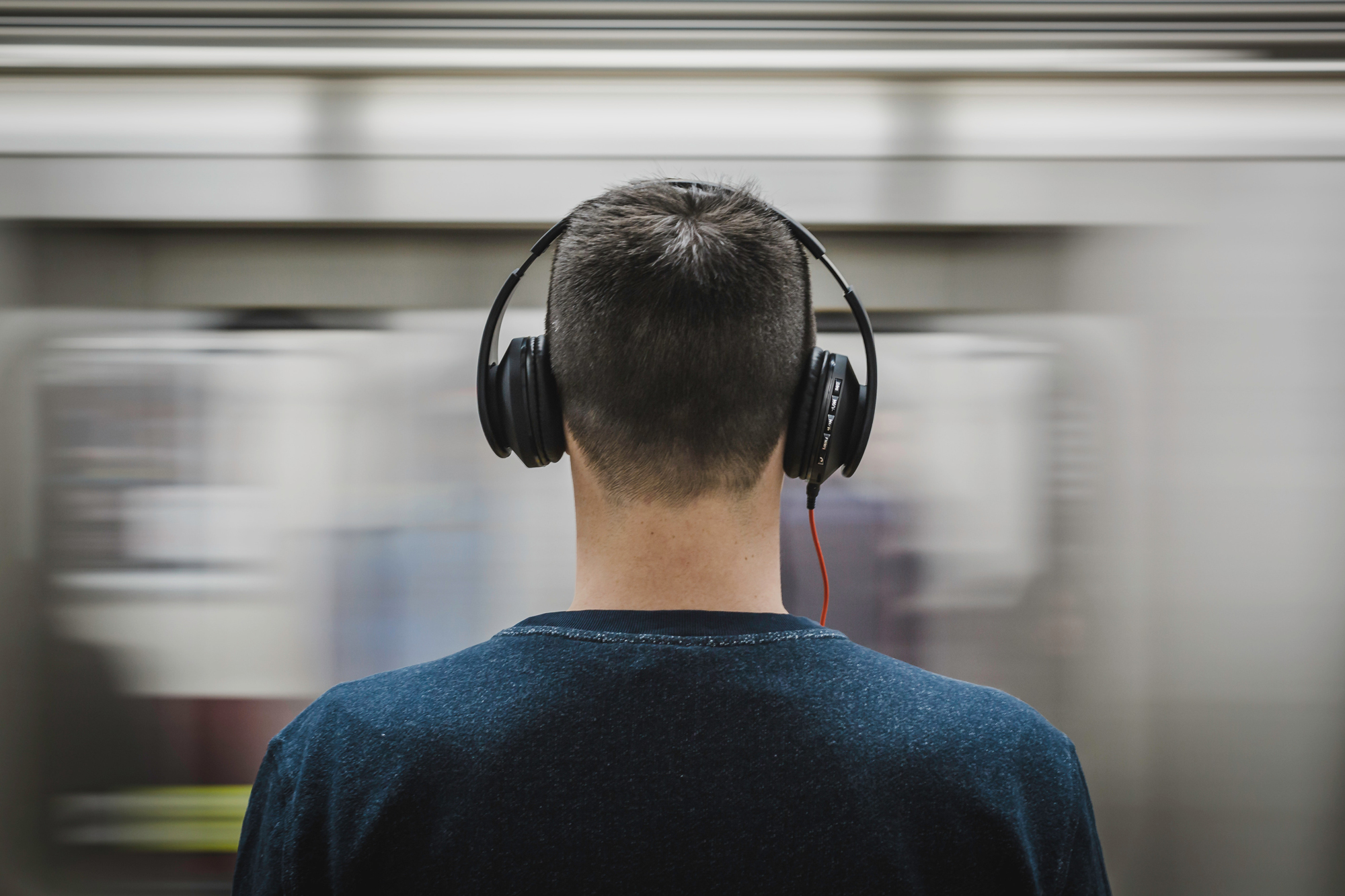 A photo of a young man wearing headphones in front of a moving train, for the article "best headphones for kids."