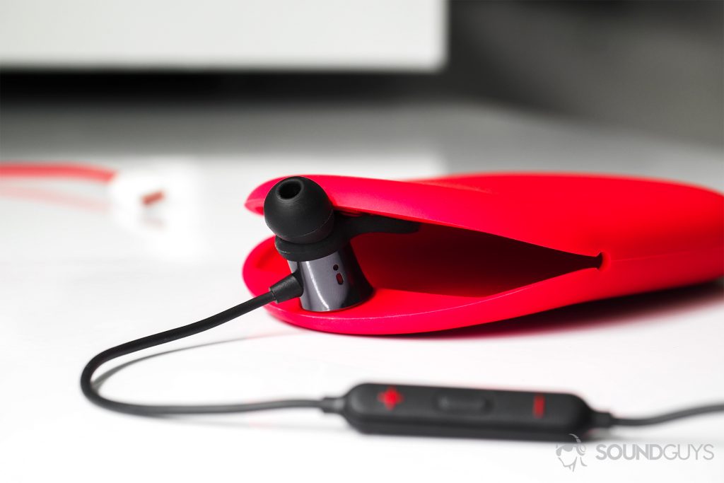 A straight-on image of the earbuds with one of them holding the opening of the carrying case open.