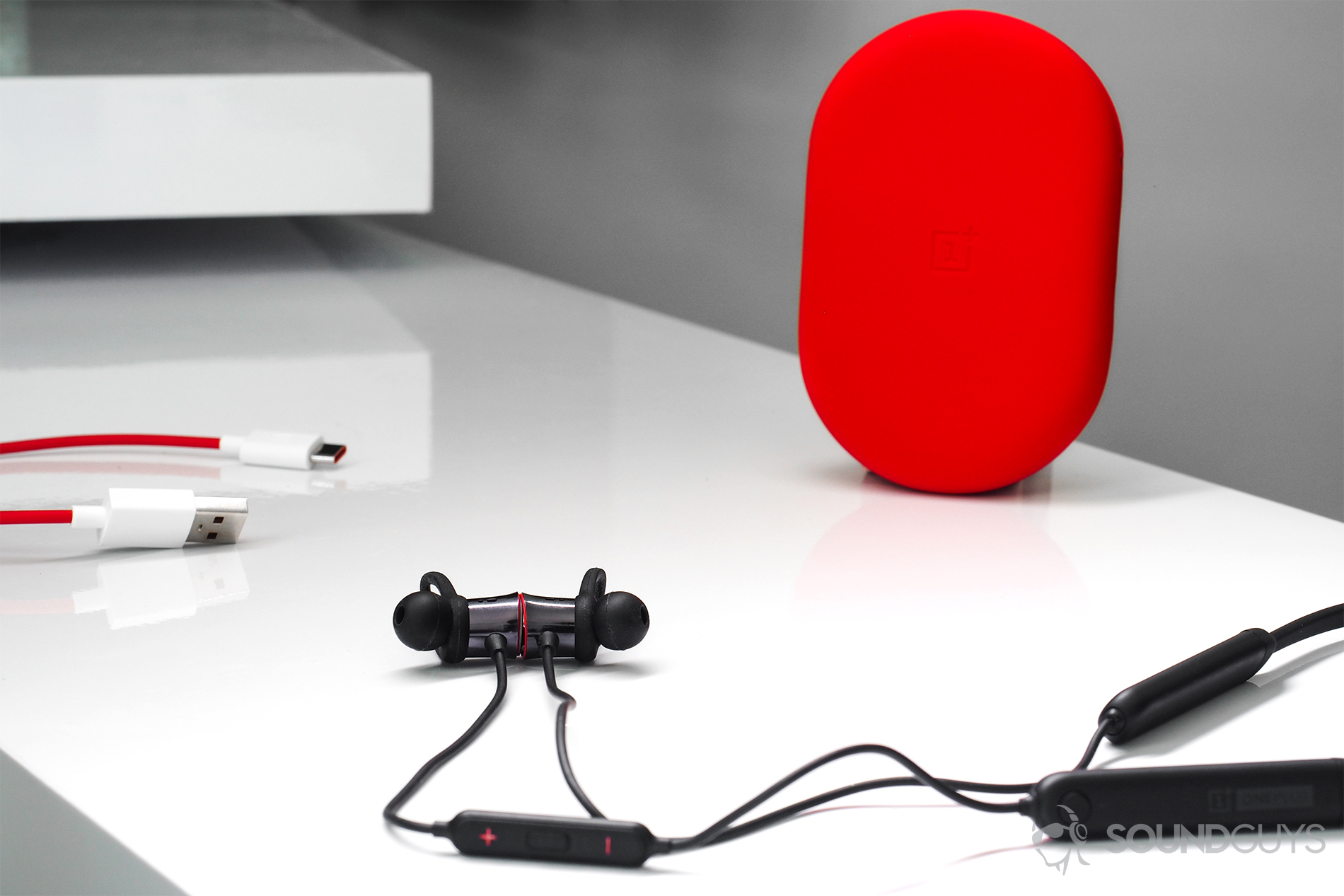 A bright image of the OnePlus Bullets Wireless earbuds with part of the neckband showing and the red carrying case standing vertically in the background.