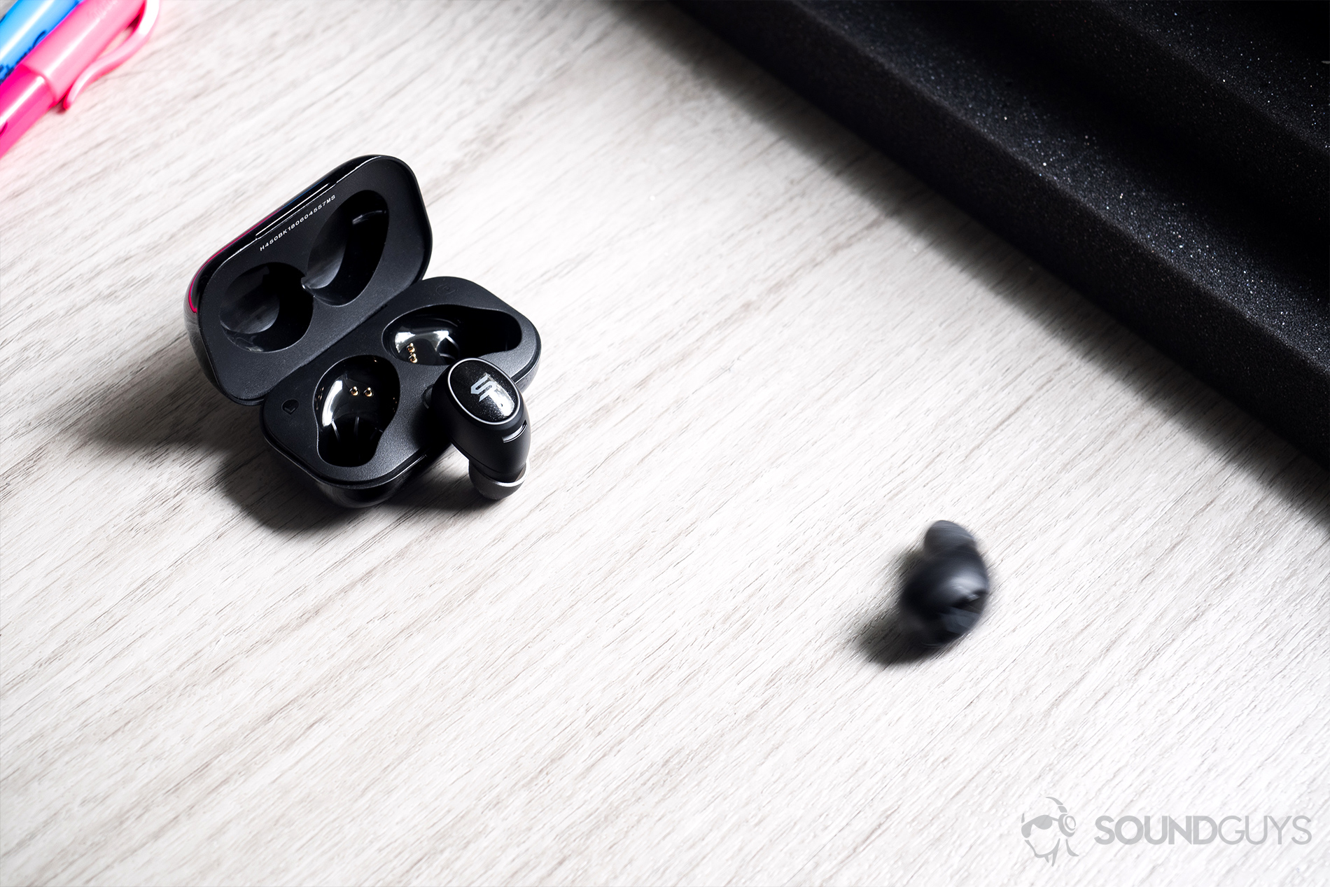 Soul Emotion: Downward angled image of one of the earbuds resting against the case (open) with the other rolling and blurred in the frame.