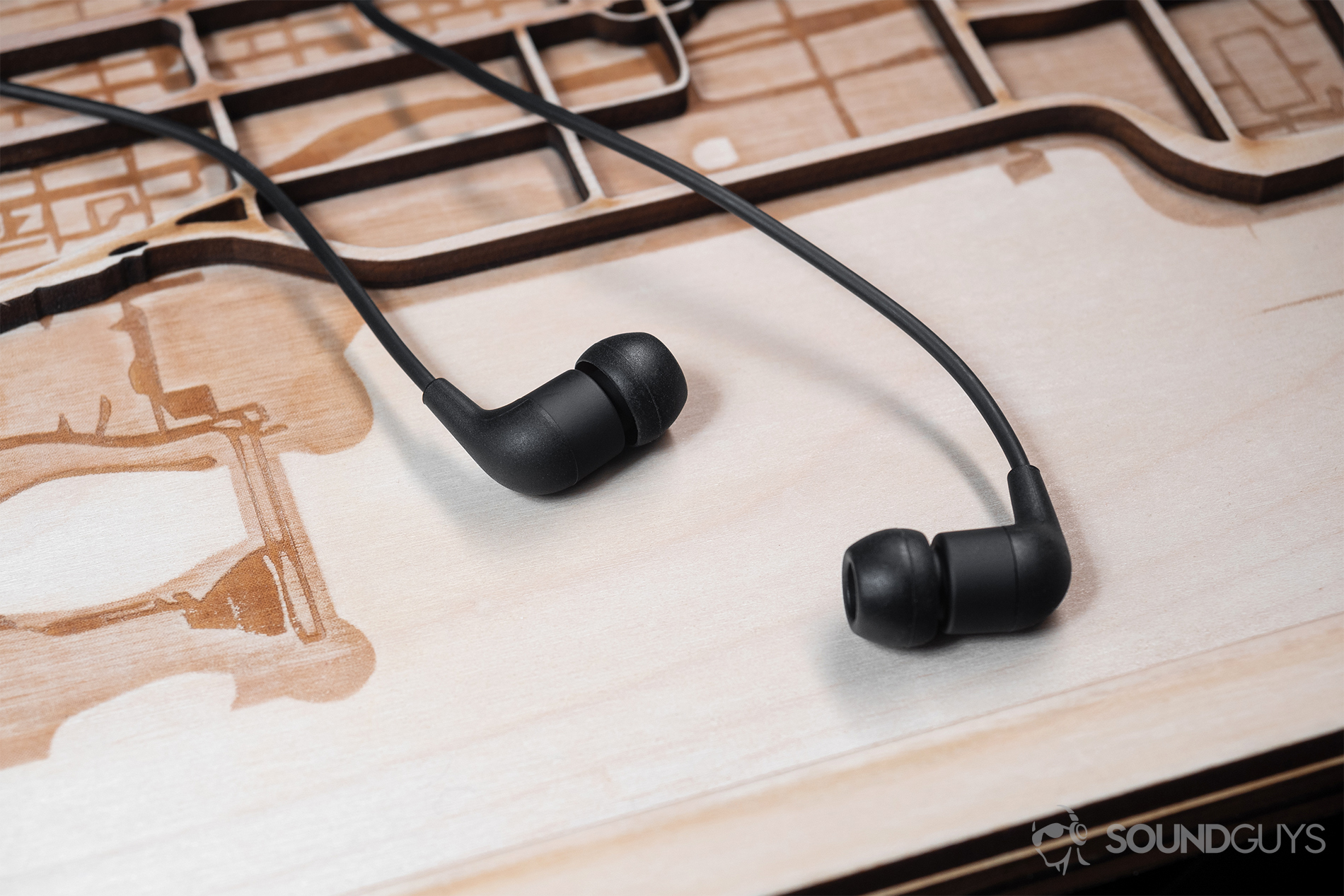 AiAiAi Pipe 2.0: Top-down image of the earbuds in black on a laser-cut wood surface.