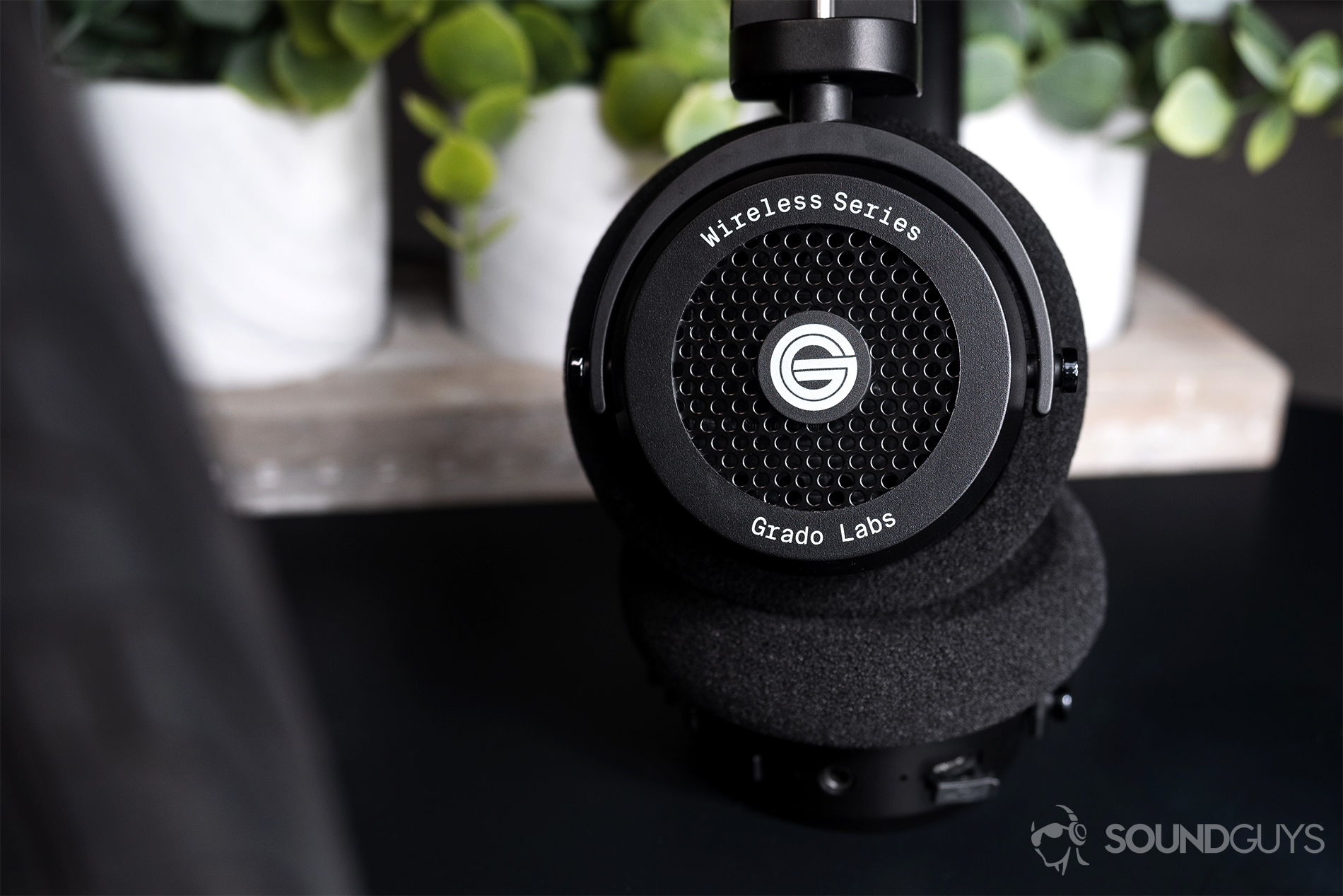 Grado GW100: The headphones standing up with one ear cup facing the camera in front of fake plants.
