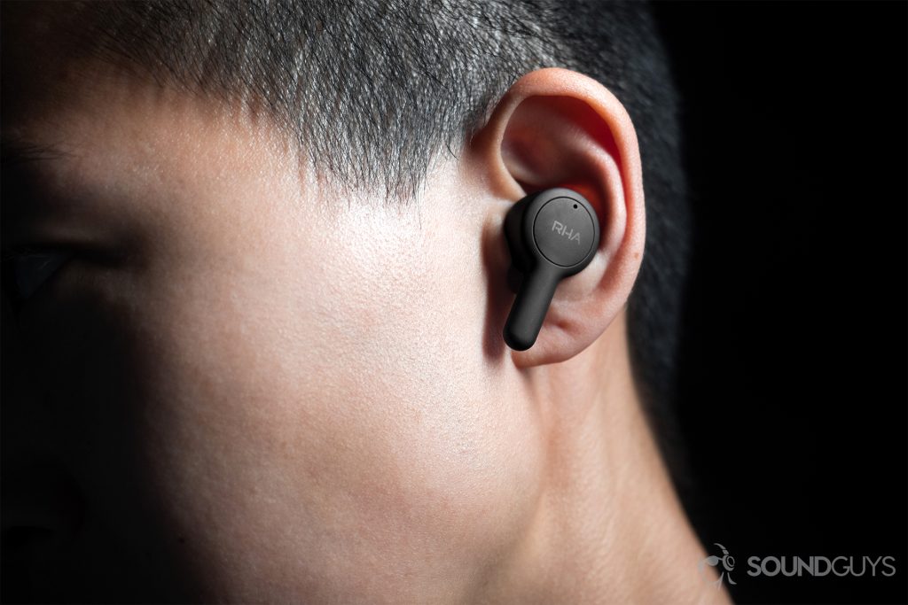 RHA TrueConnect true wireless earbuds (left) being worn by a woman, it protrudes a bit from the ear with the stem angled downward.