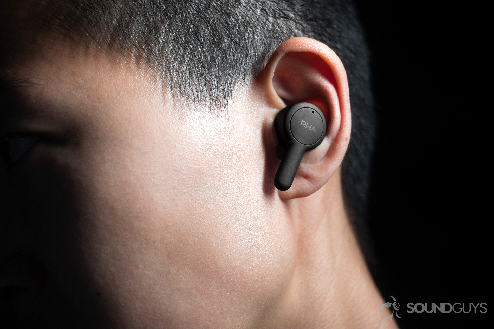 RHA TrueConnect true wireless earbuds (left) being worn by a woman, it protrudes a bit from the ear with the stem angled downward.