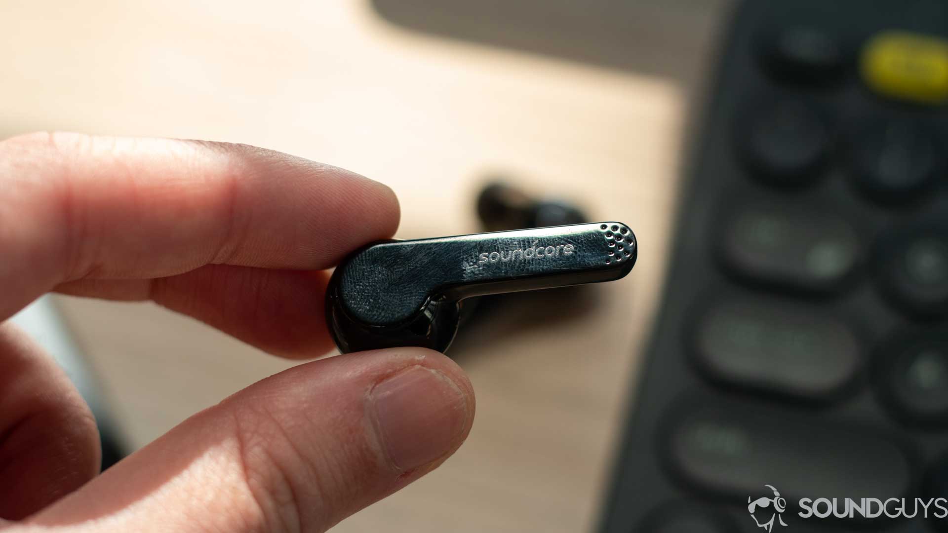 Picture of the Anker Soundcore Liberty Air earbud in hand with the Soundcore logo on the stem and the microphones visible. 
