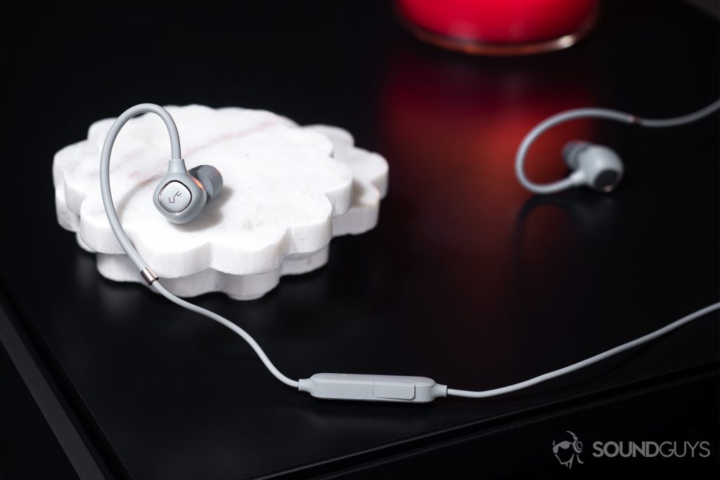 Aukey EP-B80: The earbuds on a table with one earbud resting on white coasters.