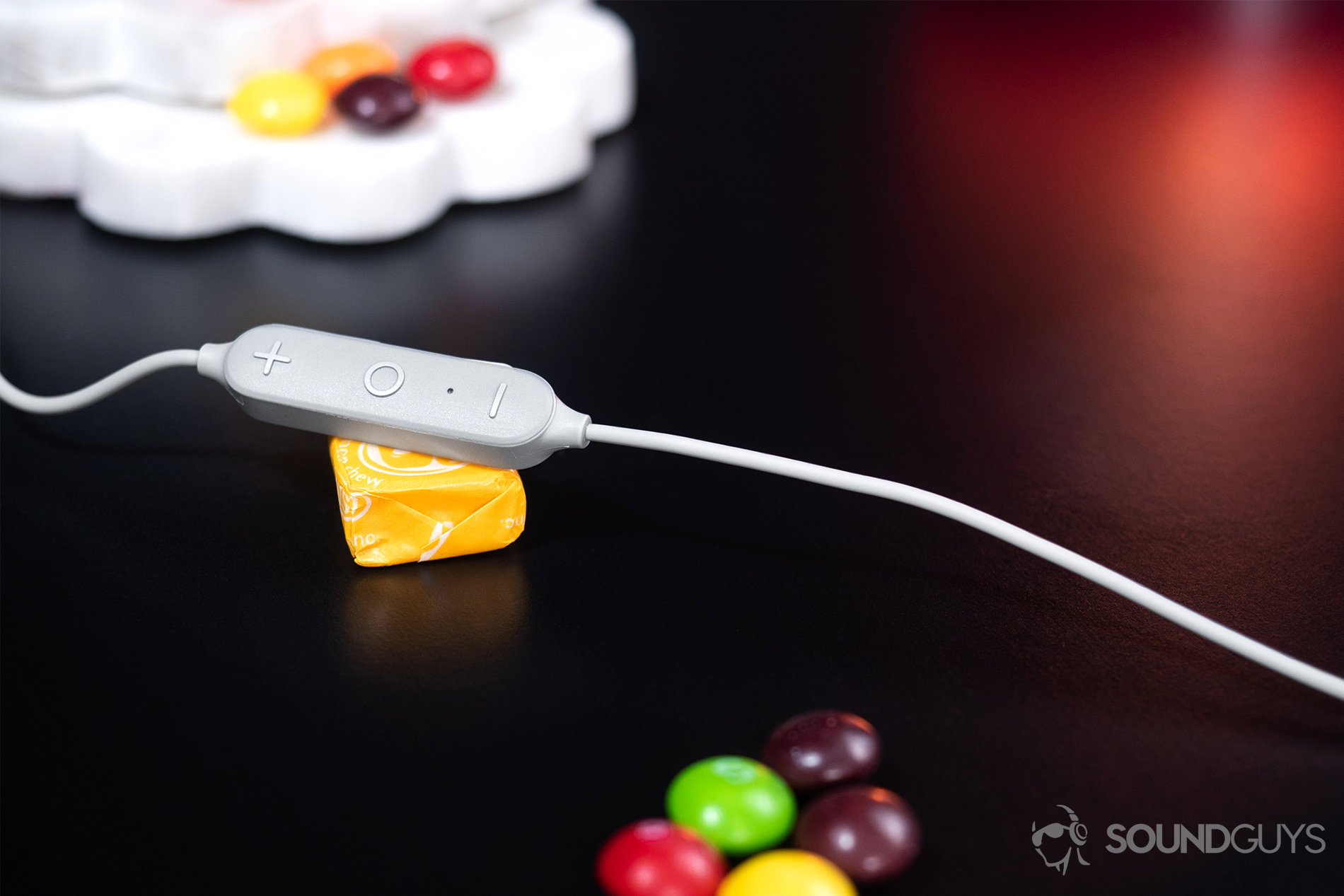 Aukey EP-B80: The integrated three button remote module resting on a yellow Starburst with Skittles scattered through the frame.