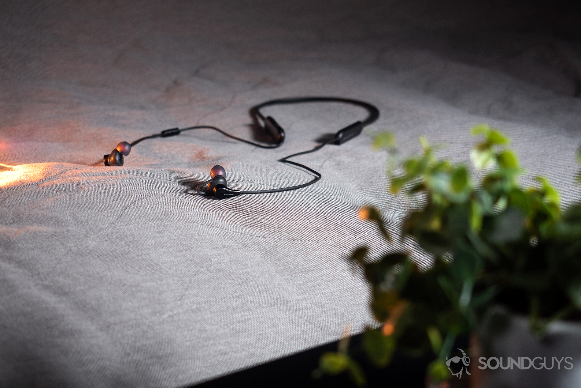 Phiaton Curve BT 120 NC: An image of the neckband earbuds laying on a grey cloth surface with light leaking in from the left vertical frame.