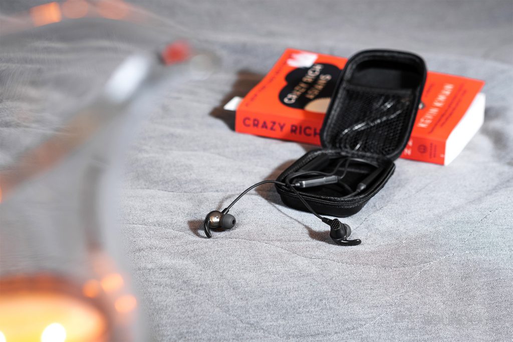 SoundPeats Engine: An image of the neckband earbuds in the case leaning against an orange book with the earbuds and cables extending from the open case.