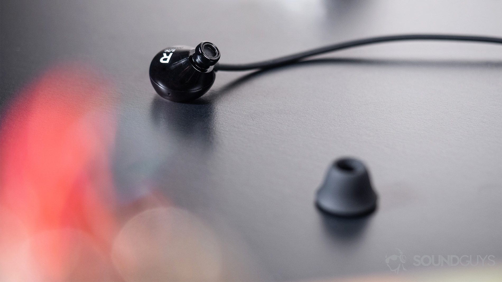 Beyerdynamic Blue Byrd: The earbuds on a black surface with a blurred out red spot on the bottom-left corner of the image.