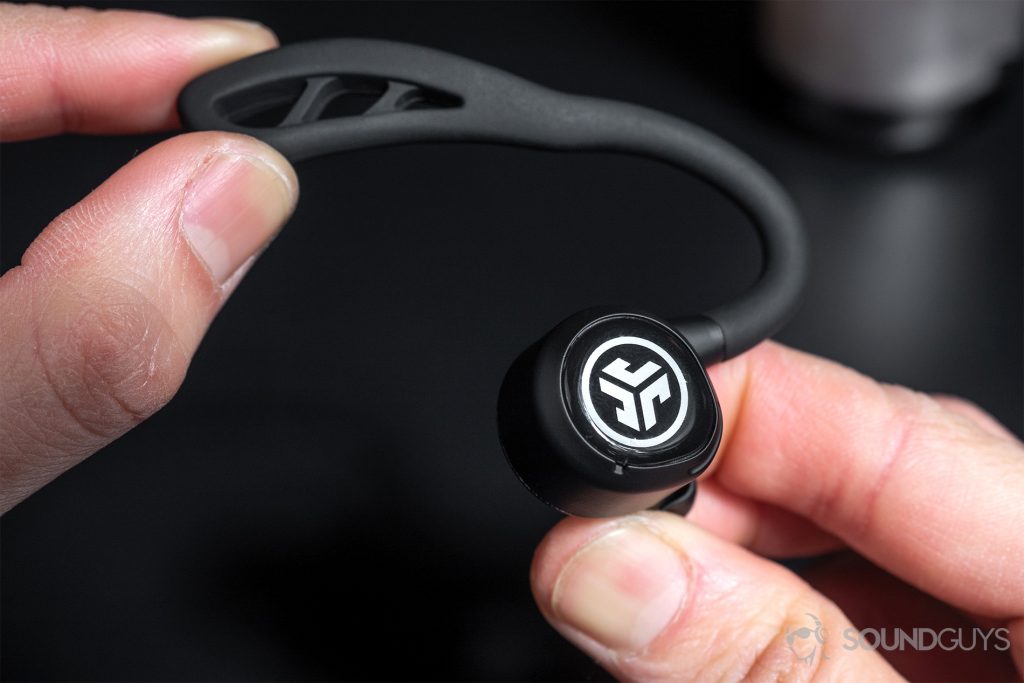 An earbud between two hands with the ear hook being bent to show flexibility.