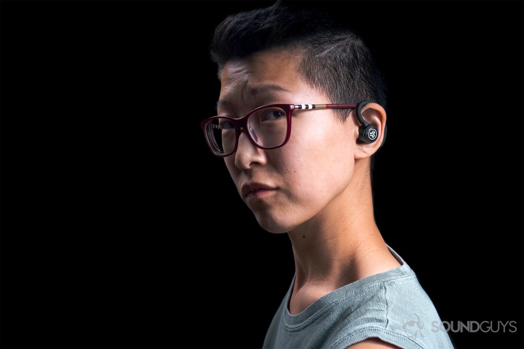 A woman wearing the JLab Epic Air Elite true wireless workout earbuds against a black background.