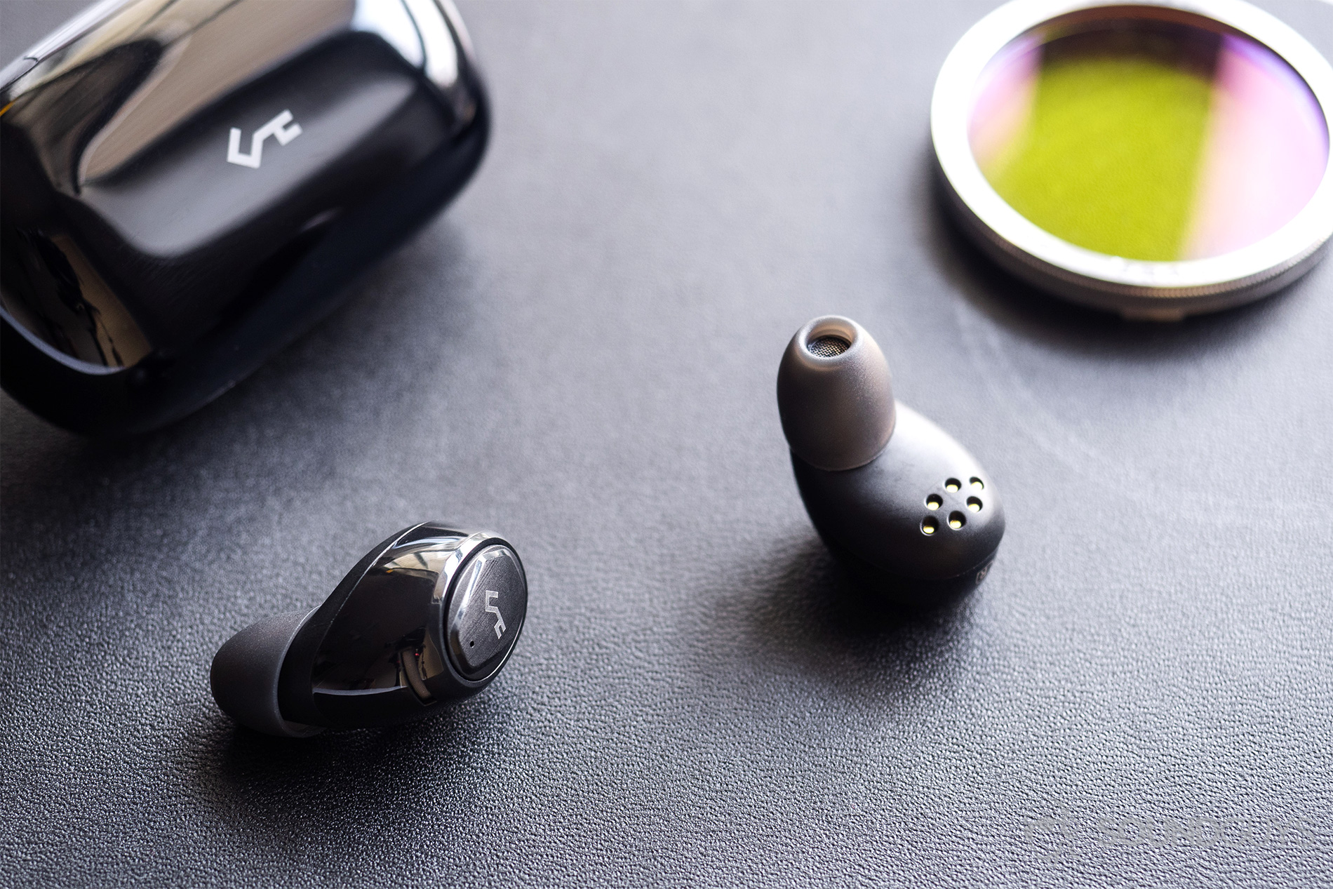 Aukey EP-T16 review: The earbuds lying adjacent to the charging case with a lens filter in the top right corner of the image.