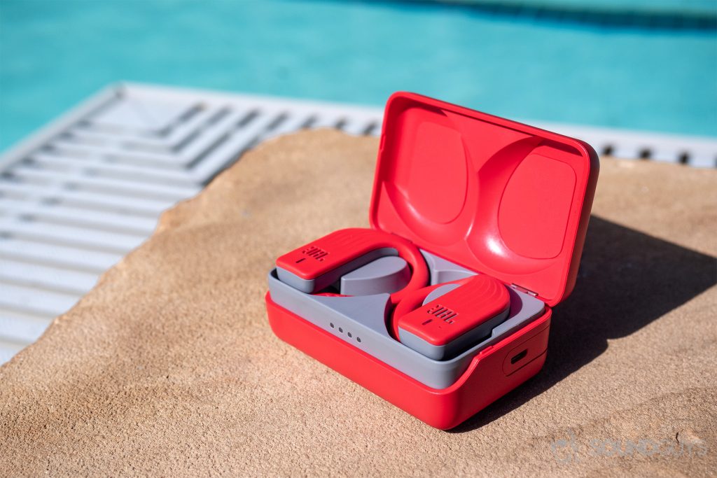 best waterproof headphones JBL Endurance Peak: The earbuds in the case on pool grounds, with a pool in the background.