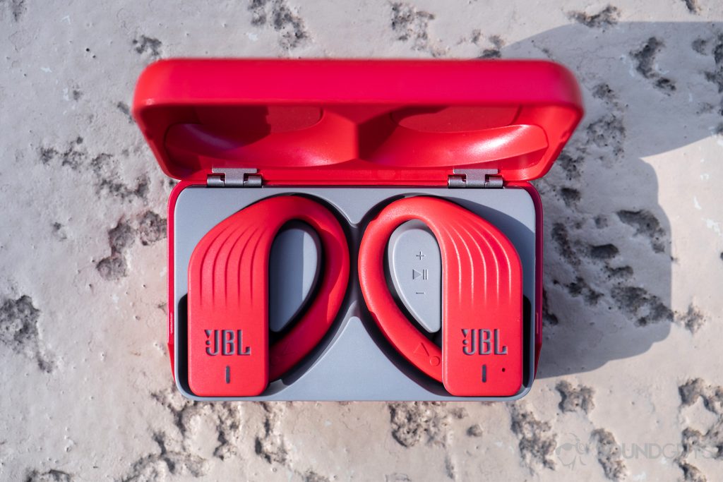 JBL Endurance Peak: Top-down image of the earbuds in the case on beige surface.