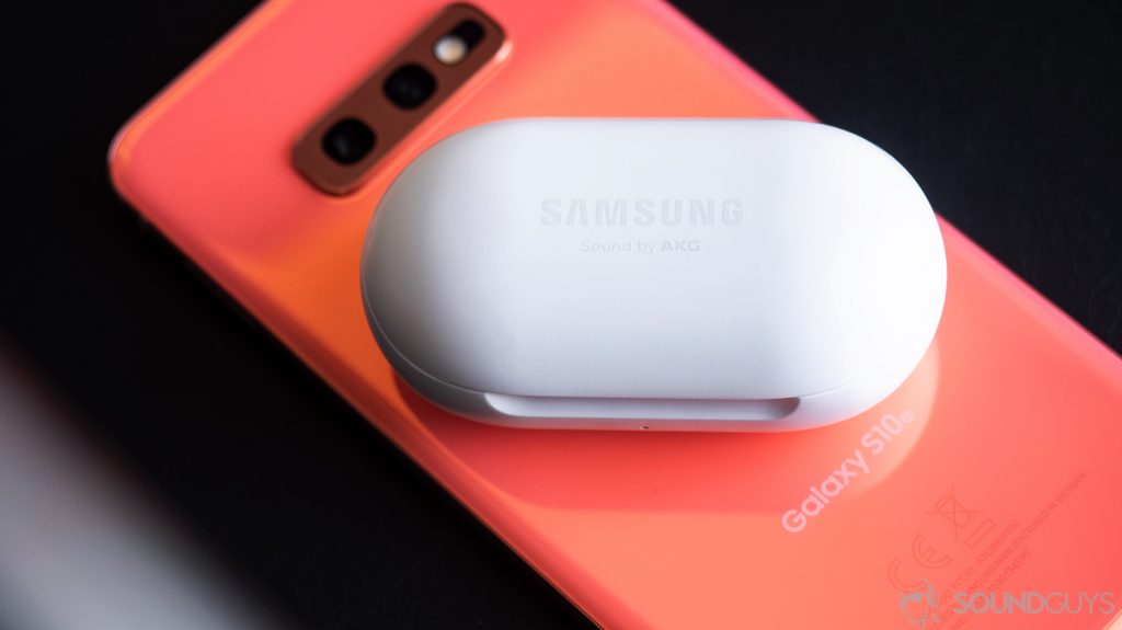 A picture of the Samsung Galaxy Buds case, which is closed, on top of a Samsung Galaxy S10e in Flamingo Pink.
