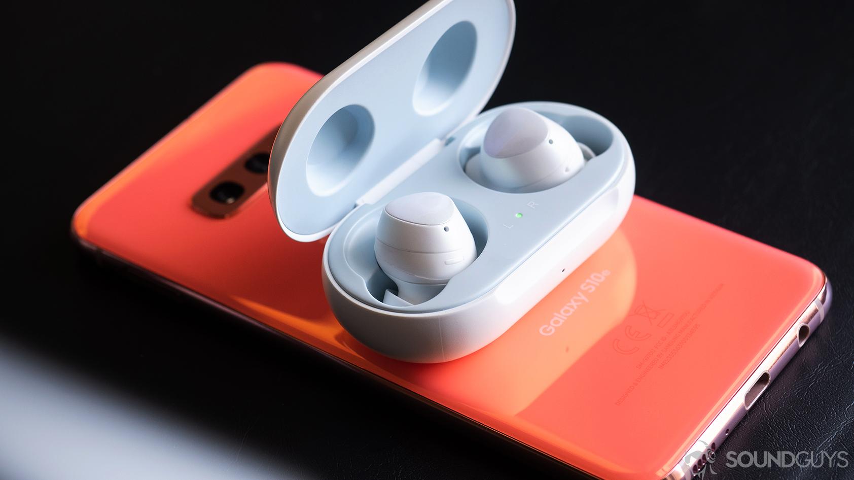 An angled photo of the Samsung Galaxy Buds in the case on top of a Samsung Galaxy S10e in Flamingo Pink.