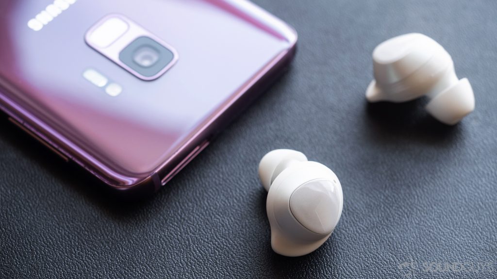 Angled image of the Samsung Galaxy Buds earbuds in front of a Samsung Galaxy S9 in Lilac.