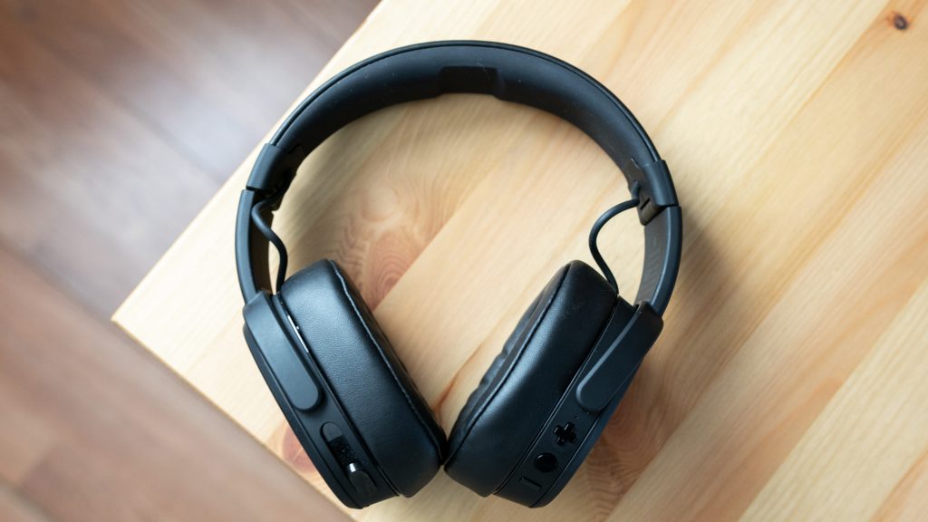 The Skullcandy Crusher Wireless in all-black on top of a wooden desk. 