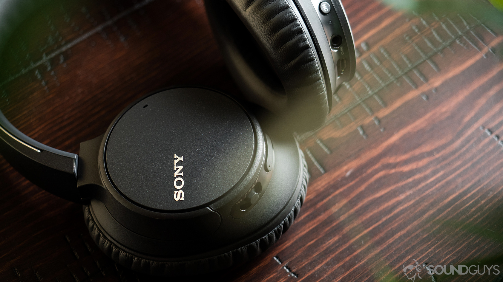 Sony WH-CH700N: Image of the headphones with one ear cup slightly rotated and the other one flat against a striated wood surface.